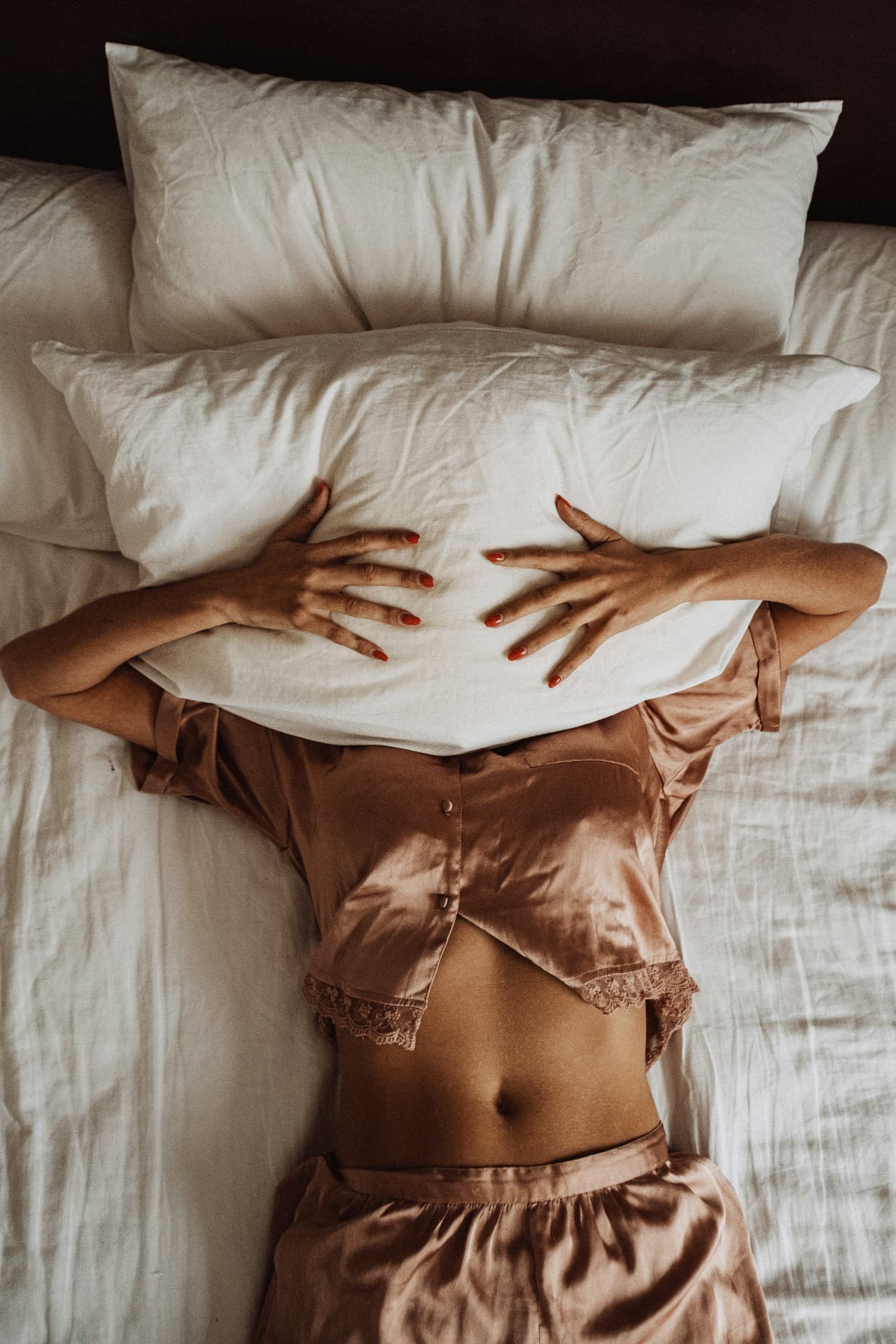 A woman lying in bed with a pillow over her face — the broken sleep and night sweats that often start in perimenopause