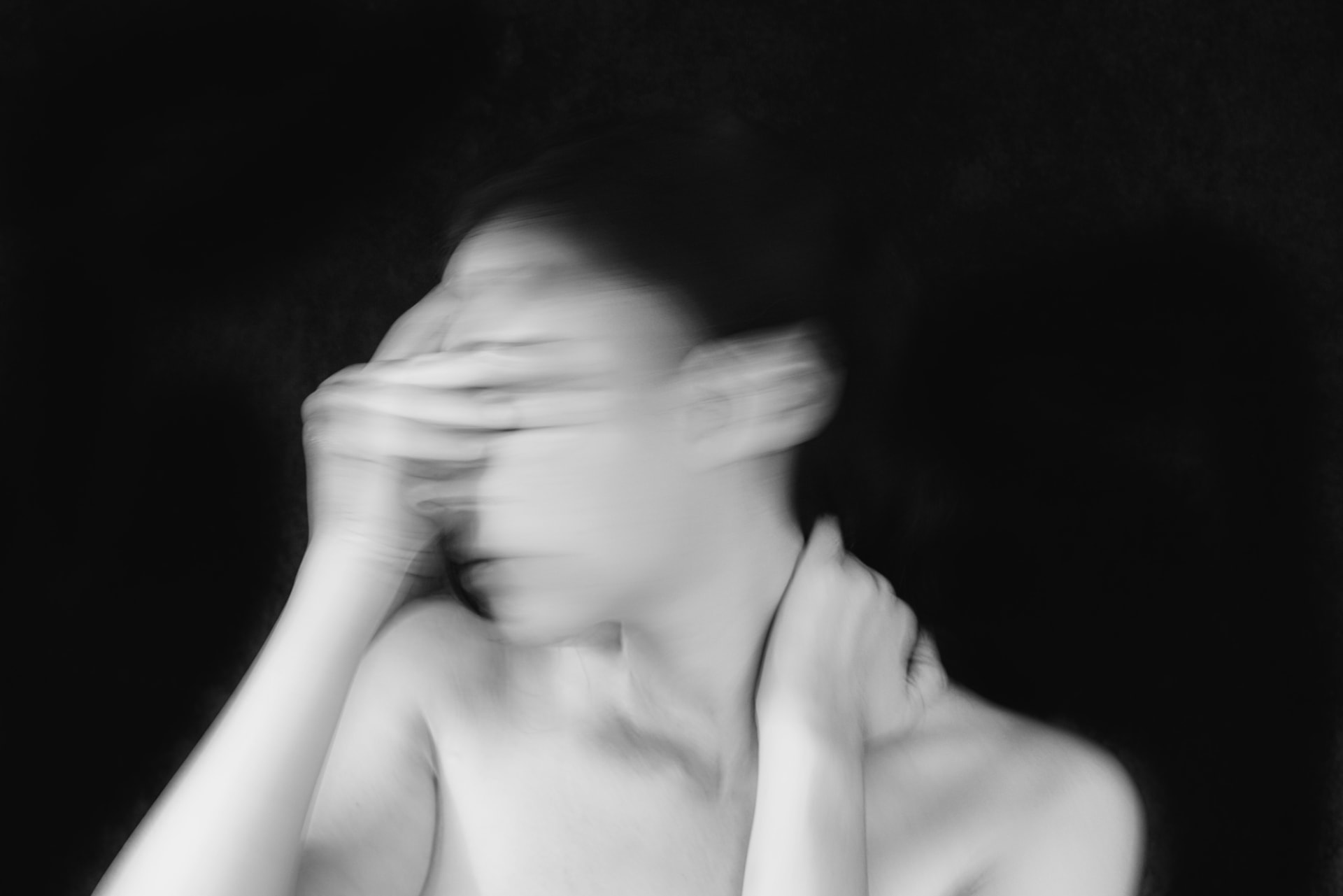 Black-and-white, motion-blurred photograph of a woman holding her head — the overwhelm and brain fog many people describe in perimenopause