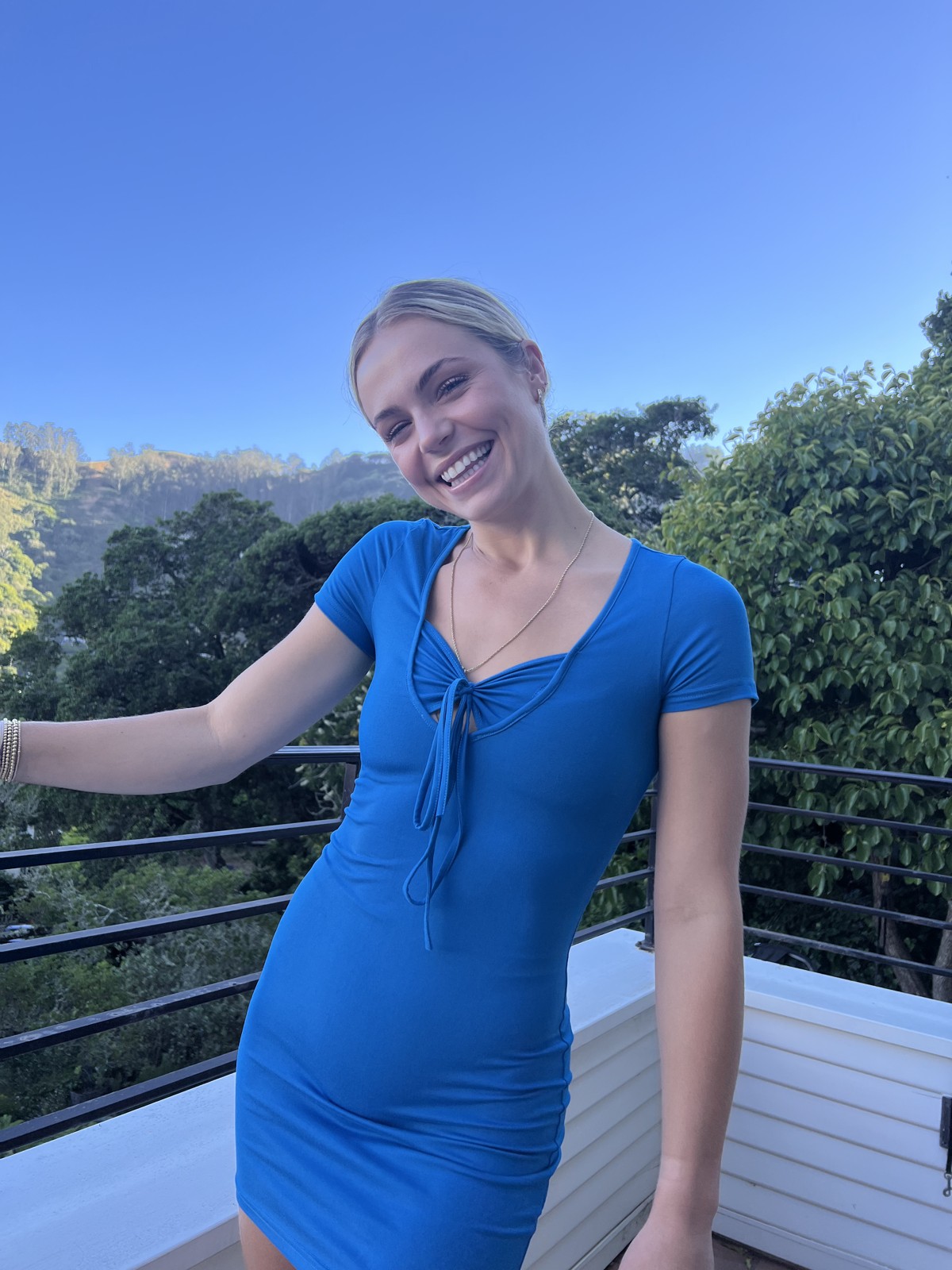 Lily smiling outdoors in a blue dress, with trees and an open sky behind her